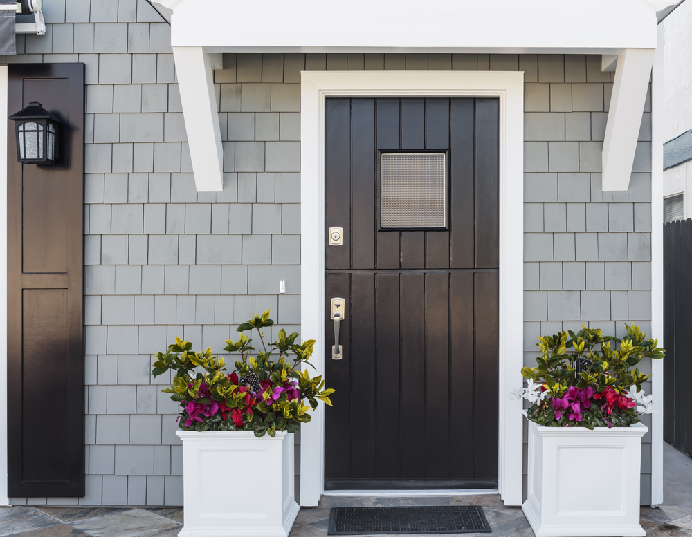 Gray house with a black front door, flanked by potted plants and accented with white exterior molding