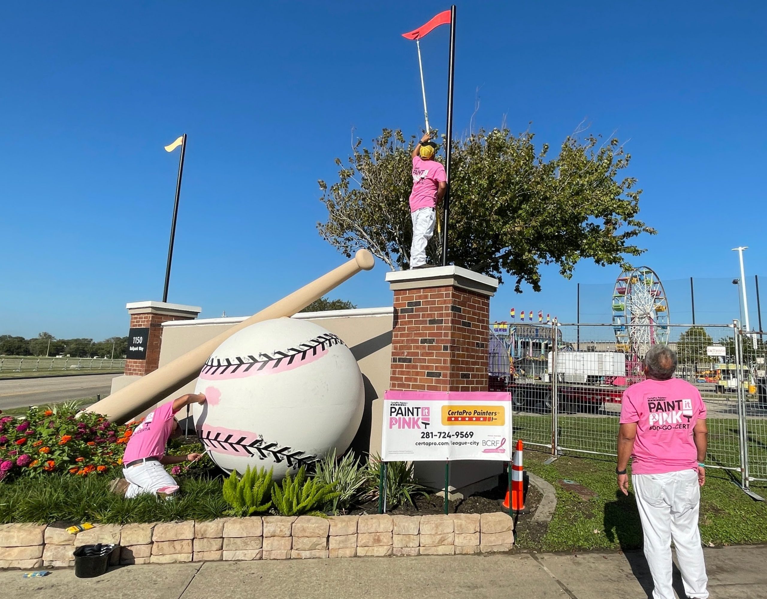 two people painting a baseball sculpture pink