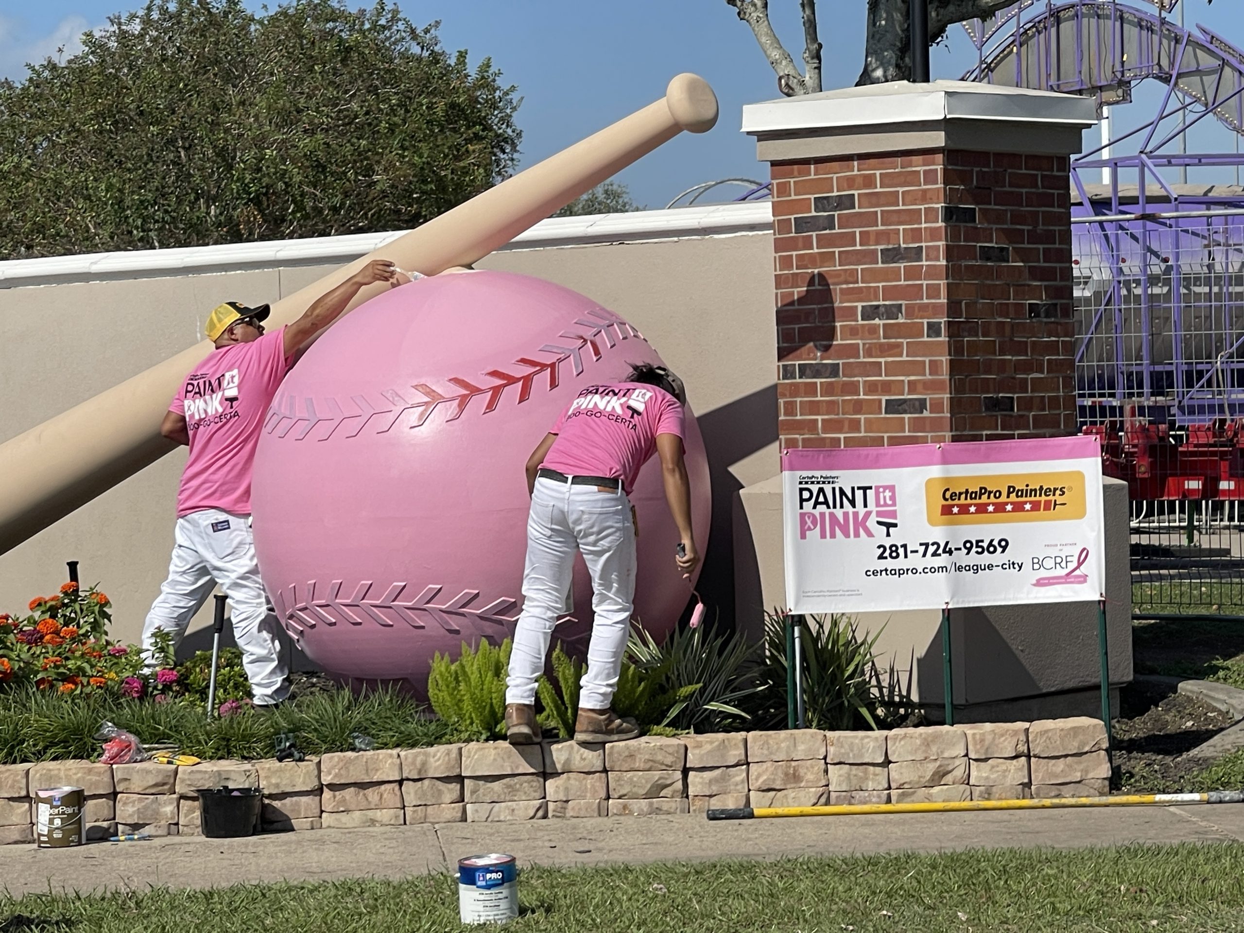 two people painting a baseball sculpture pink
