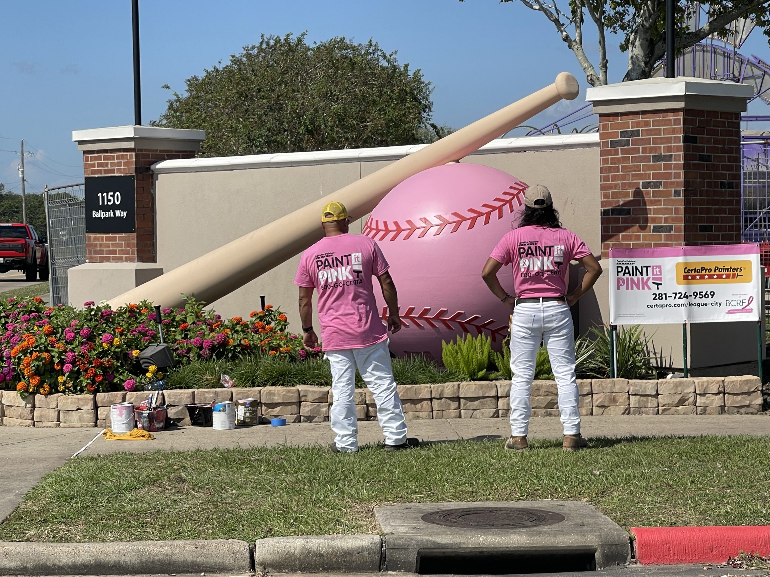 two people wearing pink shirts in front of painted baseball sculpture