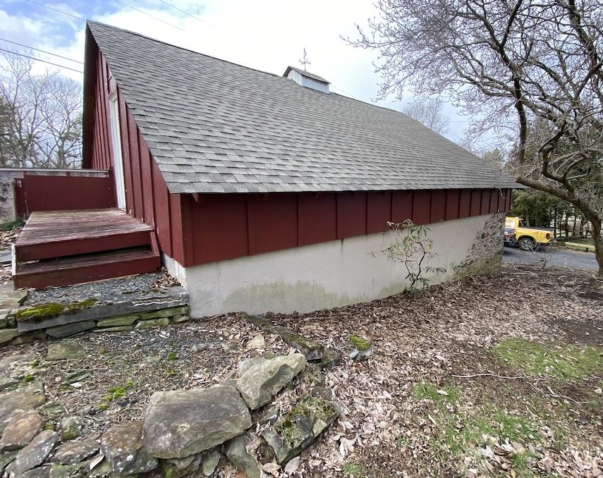 side of barn with grey roof and maroon paint on wood