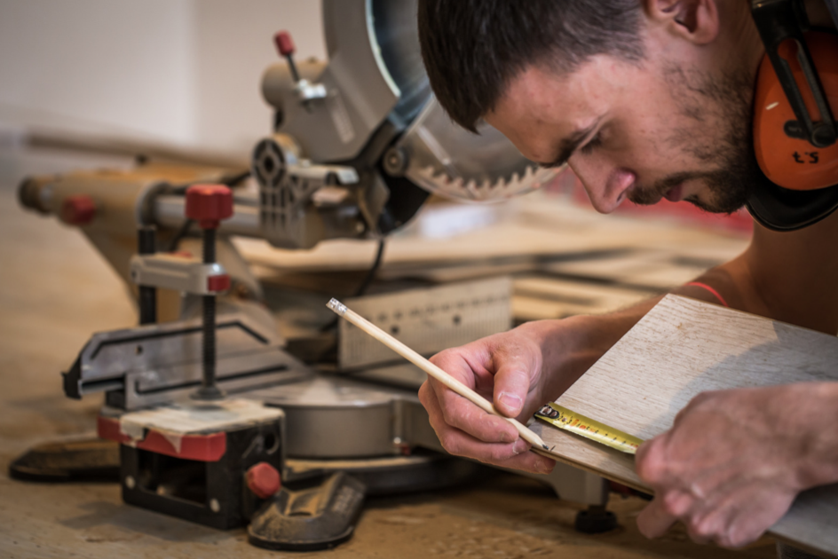 Carpenter measuring wood with electric saw in background