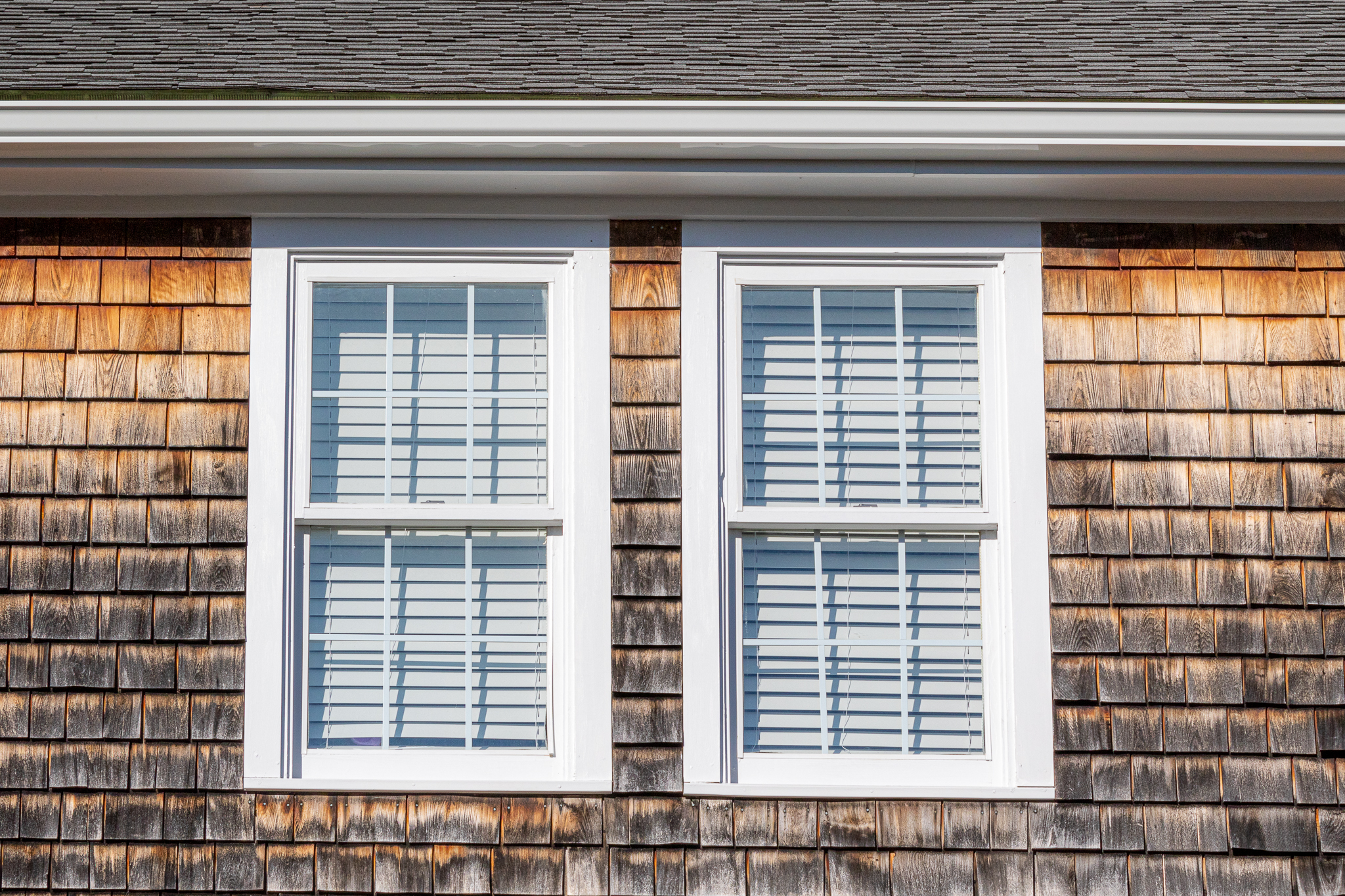 cedar shingle siding with tannins seeping through with two windows painted white