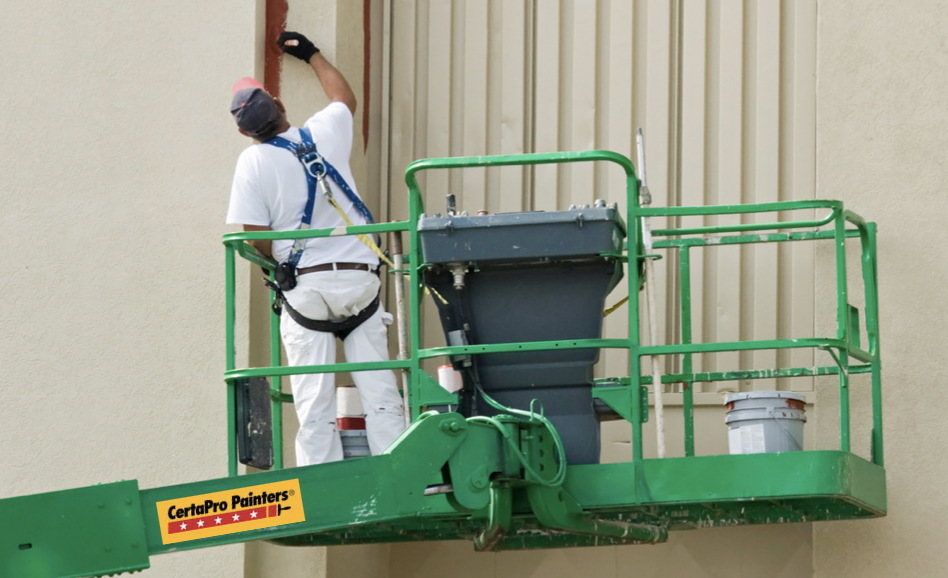 Painter on top of CertaPro Painters' branded lift painting a building from beige to a darker maroon