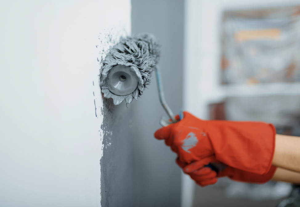 Paint roller painting a blue gray wall white.