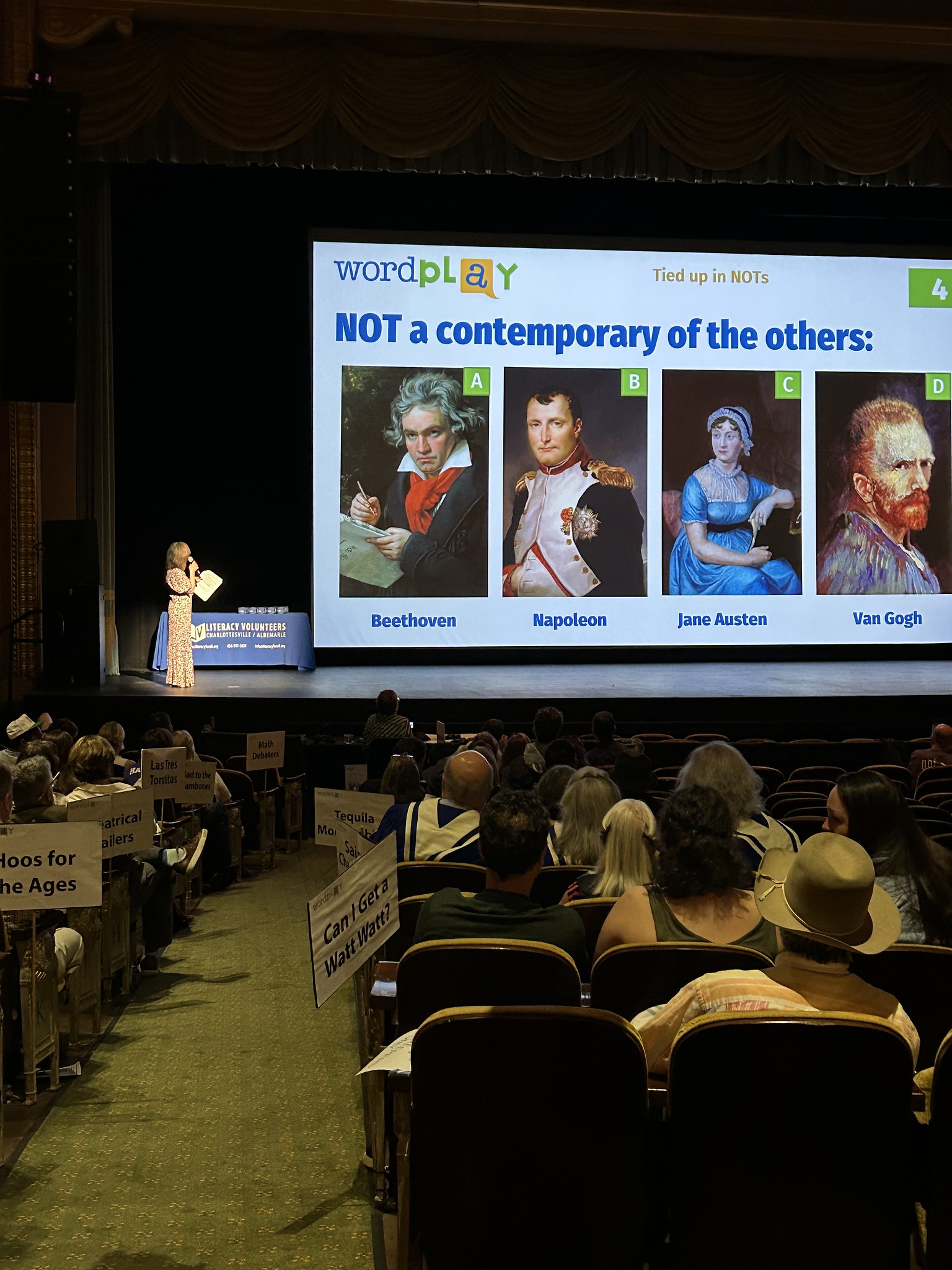 woman on stage in auditorium with quiz question on projector screen