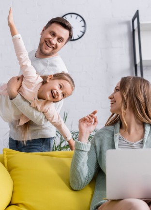 woman sitting on couch, man holding laughing child