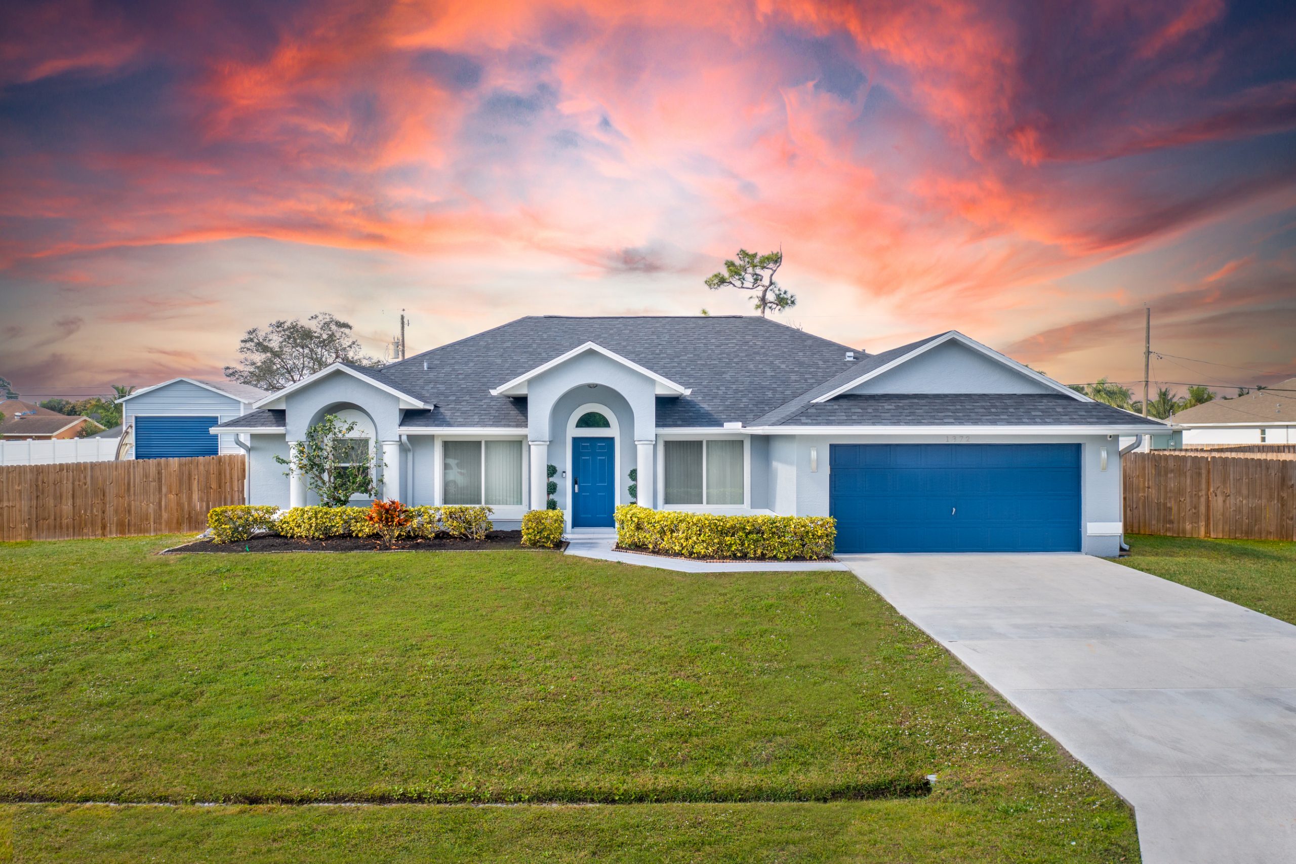 "After" image of a white house freshly painted in Florida with blue accents, a fresh cut lawn, and sunset.