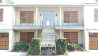 sidewalk view of residential property with stained wood garage doors and window shutters