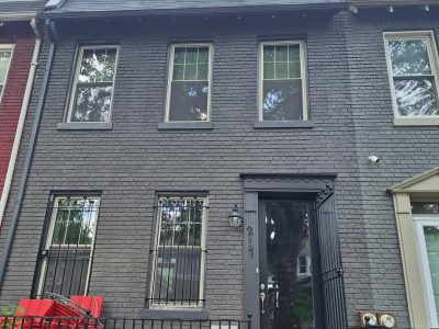 front exterior of grey painted brick townhouse with black door and trim