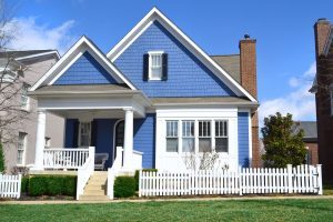 Blue home with black shutters and white trim and a white picket fence