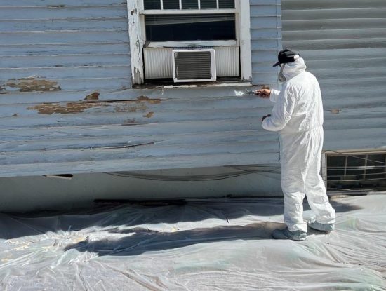 person in hazmat suit scraping lead paint from house exterior